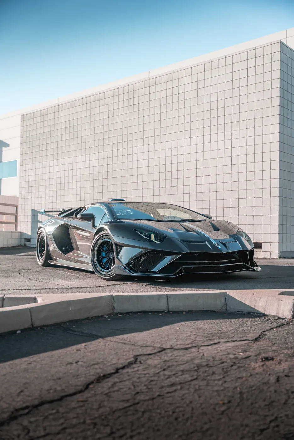 A wide-body Lamborghini Aventador against a white warehouse wall.