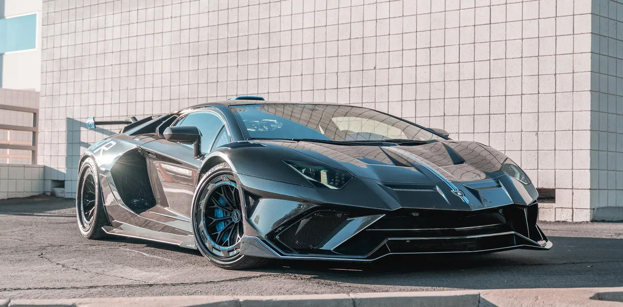 A wide-body Lamborghini Aventador against a white warehouse wall.