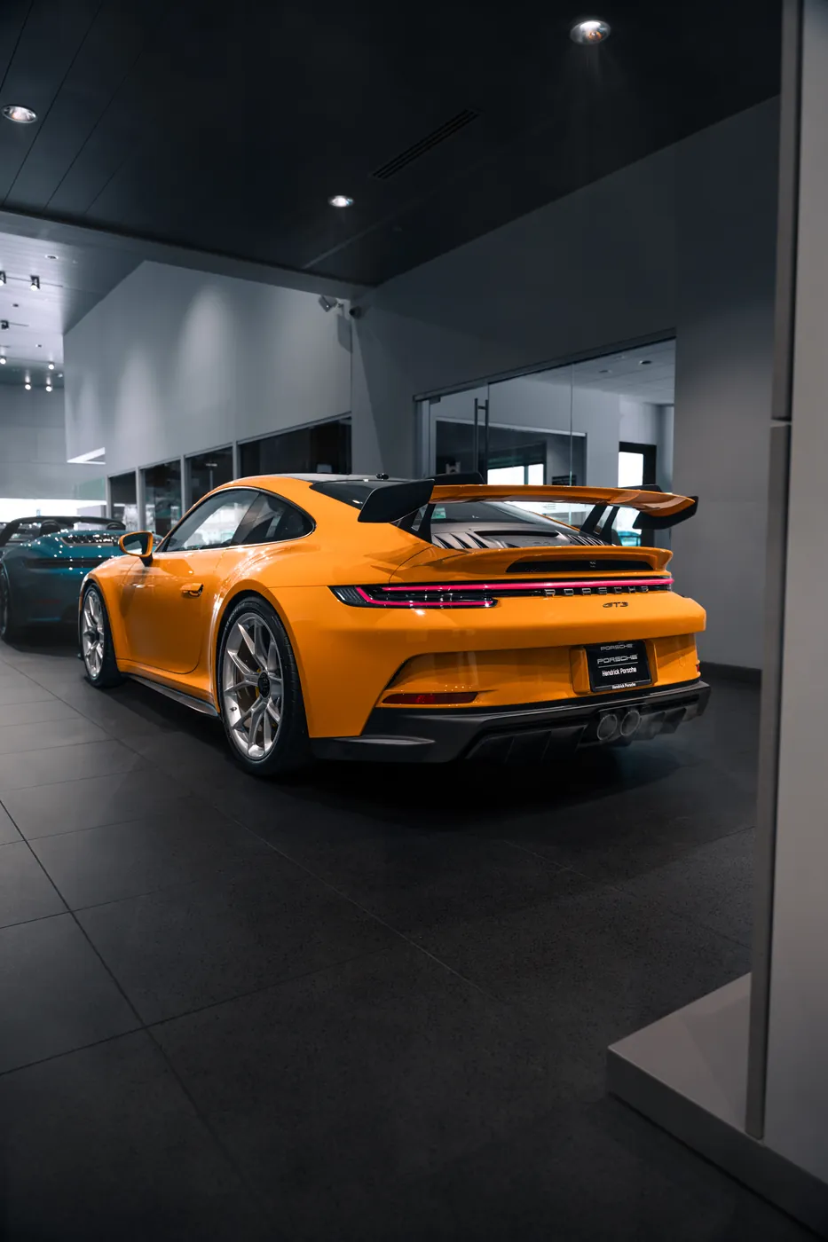An orange Porsche 911 GT3 seen from behind on a dealership showroom floor.