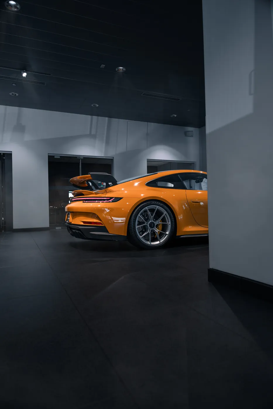 The rear quarter of an orange Porsche 911 GT3, half hidden behind a showroom wall.