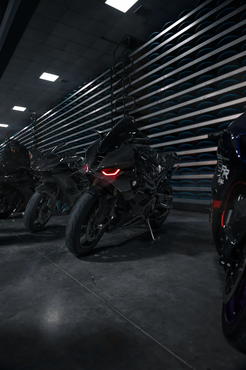 A black carbon-bodied BMW sport bike with a red LED headlight, parked in a row of motorcycles.