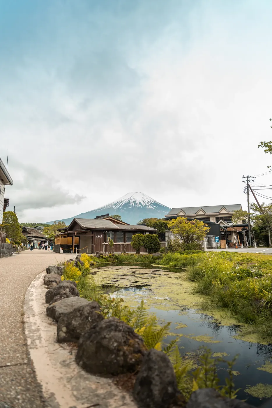 Mount Fuji rising behind a village stream and grassy bank.