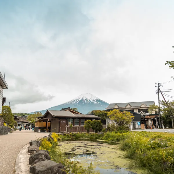 Mount Fuji rising behind a village stream and grassy bank.