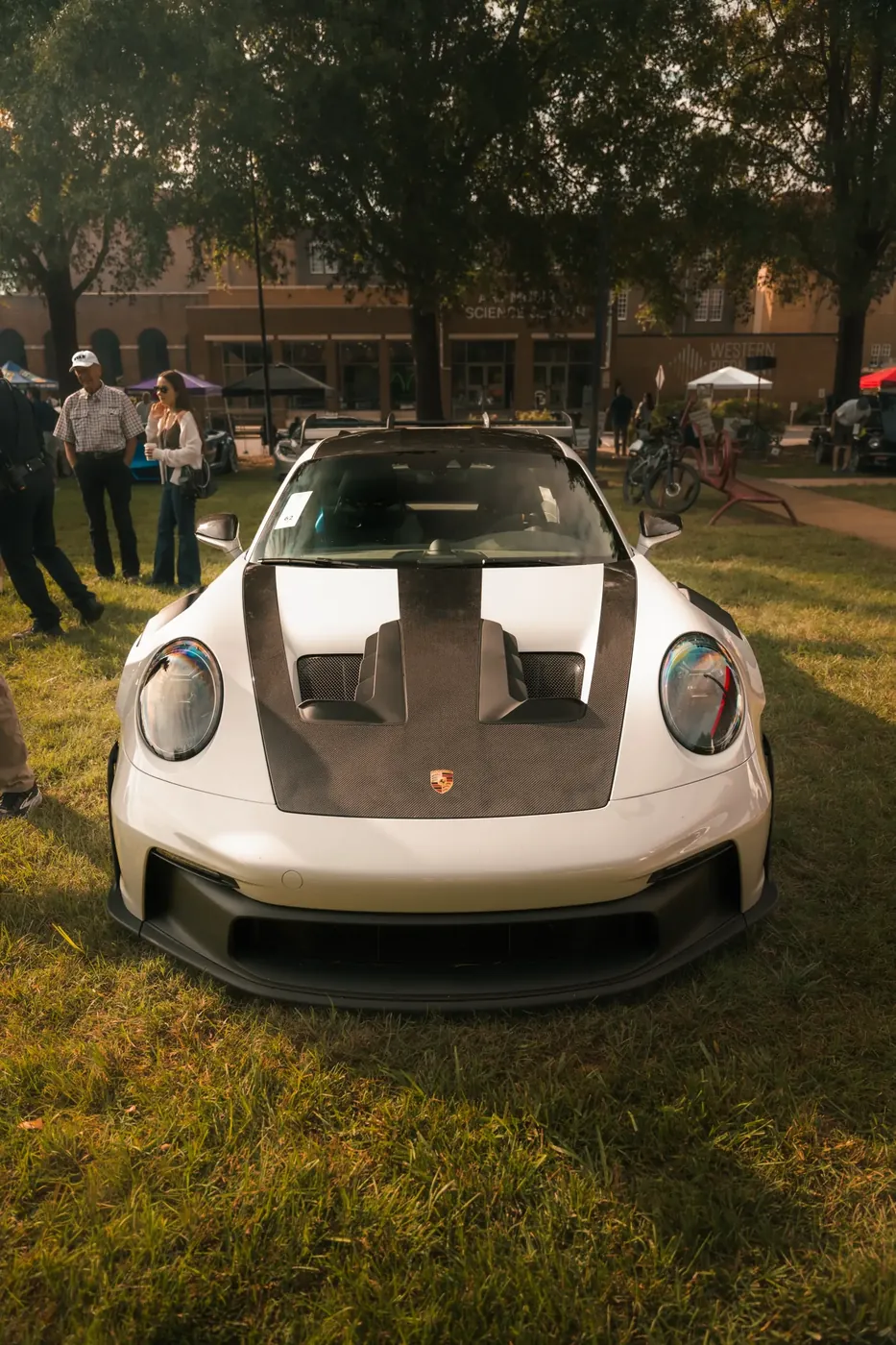 A white Porsche 911 GT3 RS with a carbon hood, shot head-on at an outdoor car show.