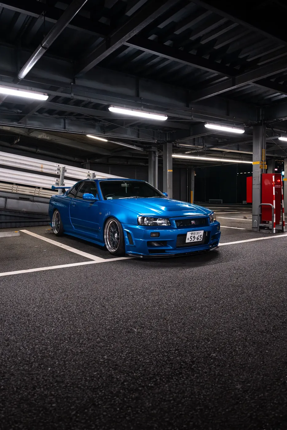 A blue Nissan Skyline GT-R in a covered parking structure.