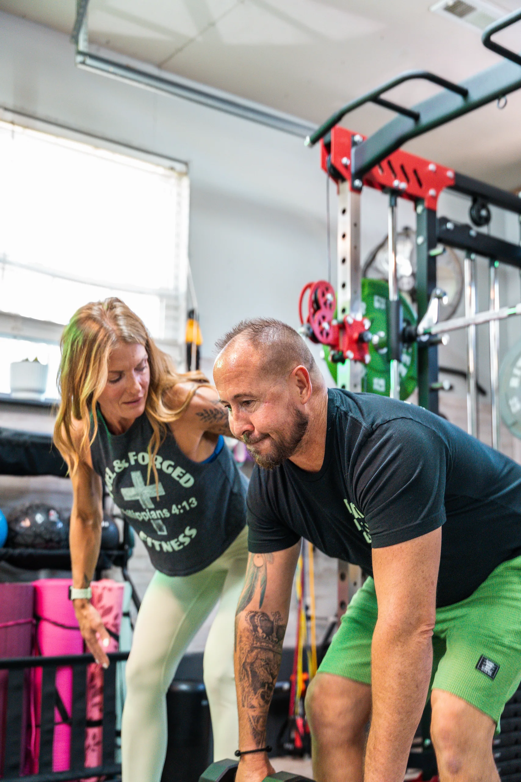 A personal trainer coaching a man through a dumbbell row in a home gym.