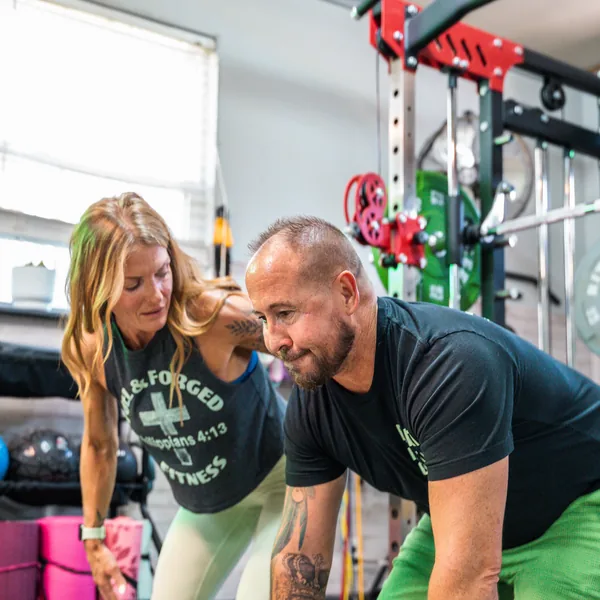 A personal trainer coaching a man through a dumbbell row in a home gym.