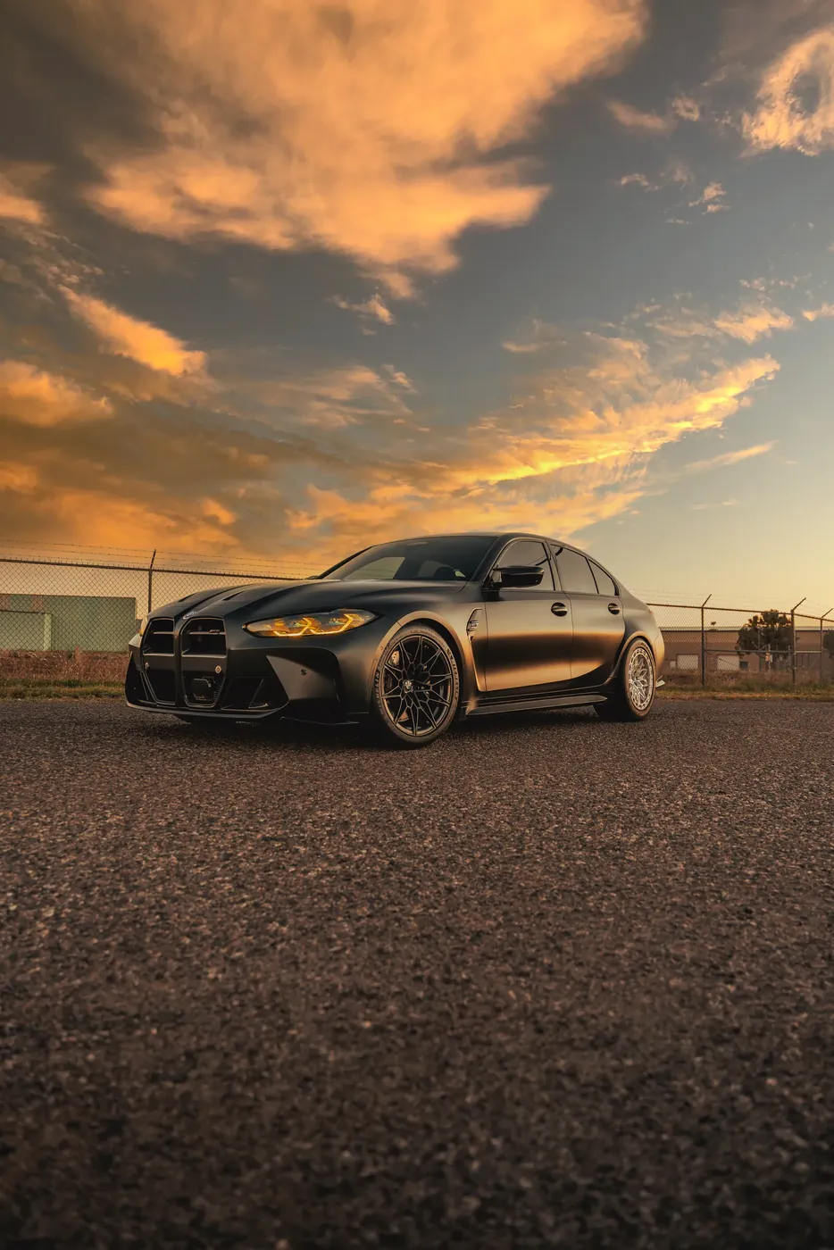 A BMW M3 photographed at sunset under a broken orange sky.