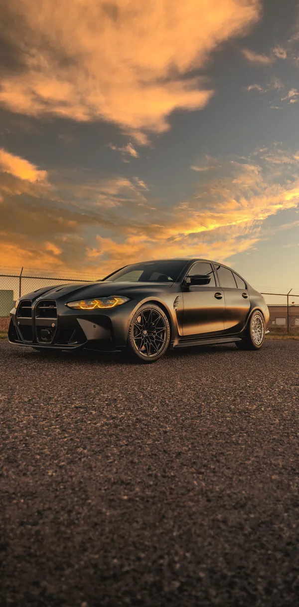 A BMW M3 photographed at sunset under a broken orange sky.
