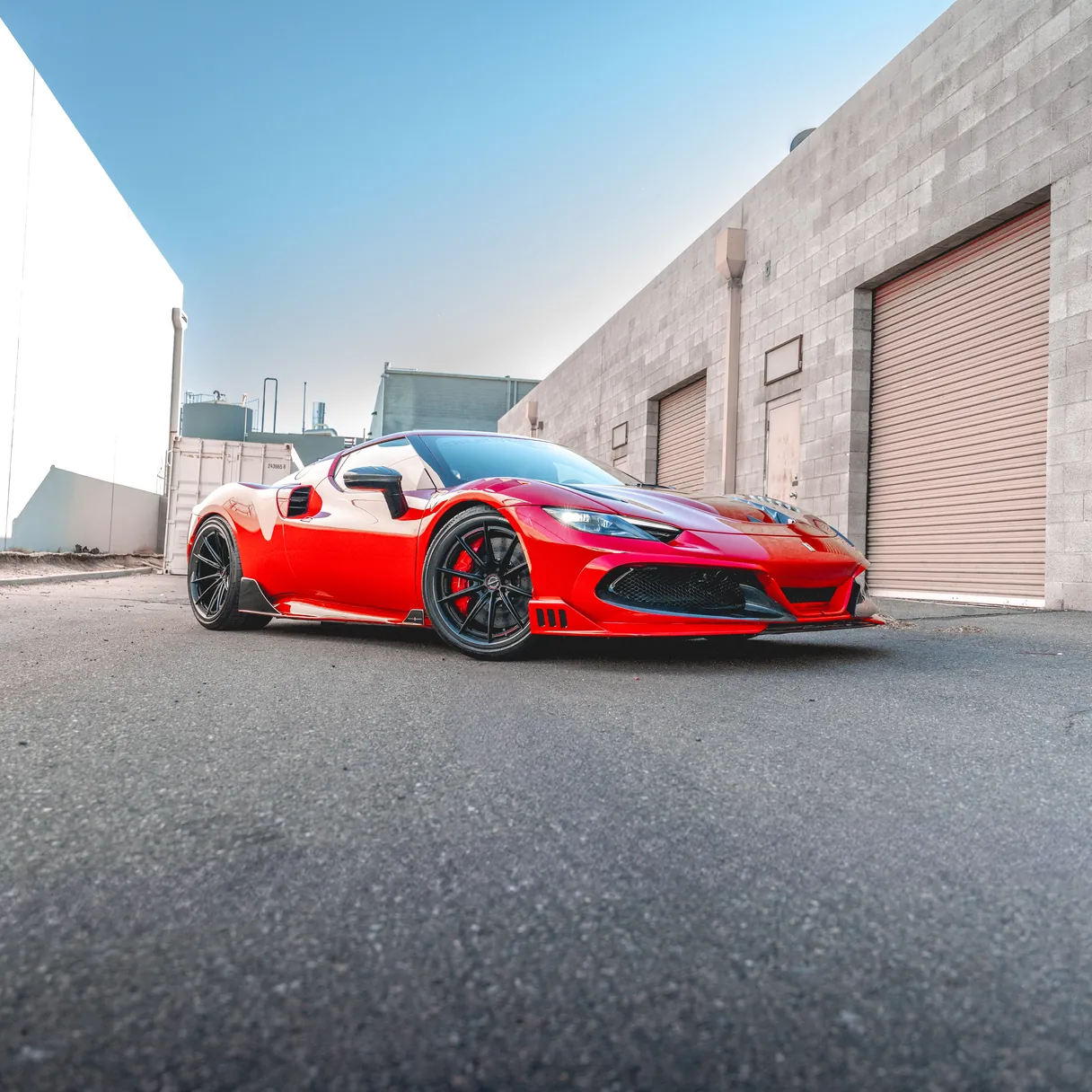 A red mid-engined sports car outside an industrial unit.