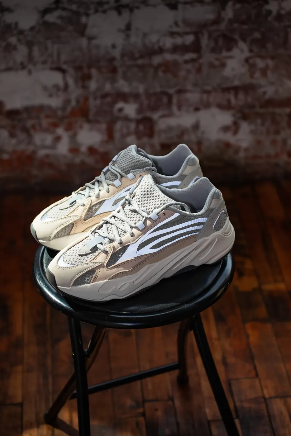 A studio product shot of a sneaker on a metal stool against brick.