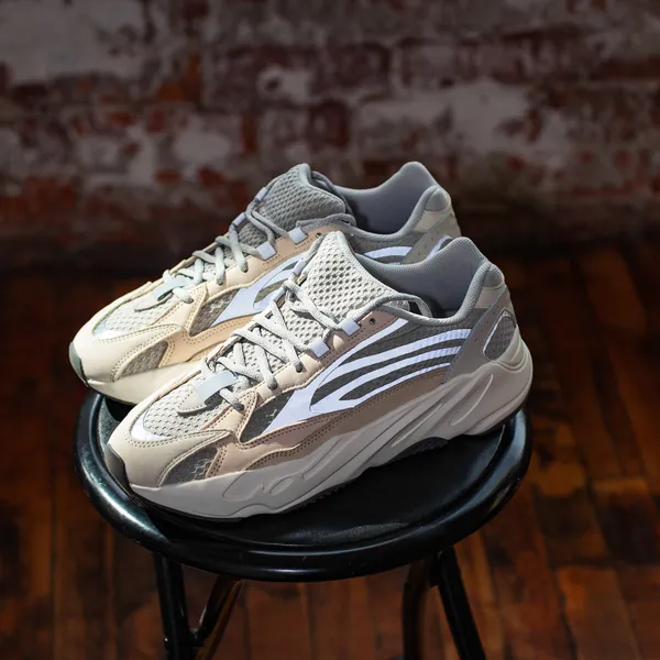 A studio product shot of a sneaker on a metal stool against brick.