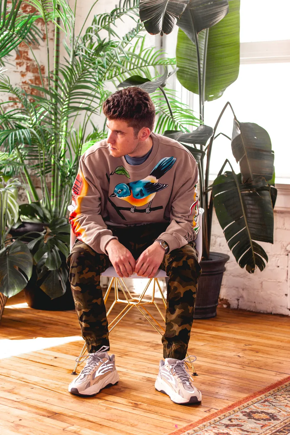 A man seated among large houseplants in a bright room.