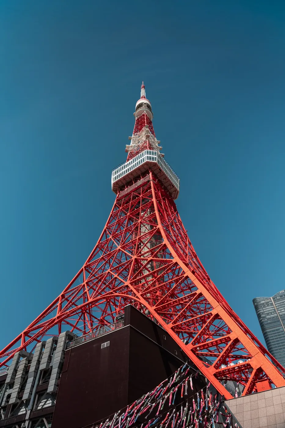 Tokyo Tower&rsquo;s red steel lattice rising into a clear blue sky, shot from directly below.