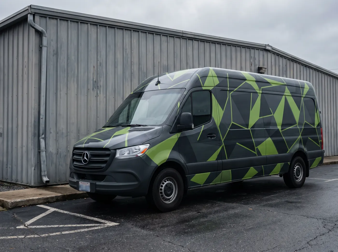 A Mercedes Sprinter van in a charcoal and lime-green geometric printed wrap outside a warehouse.