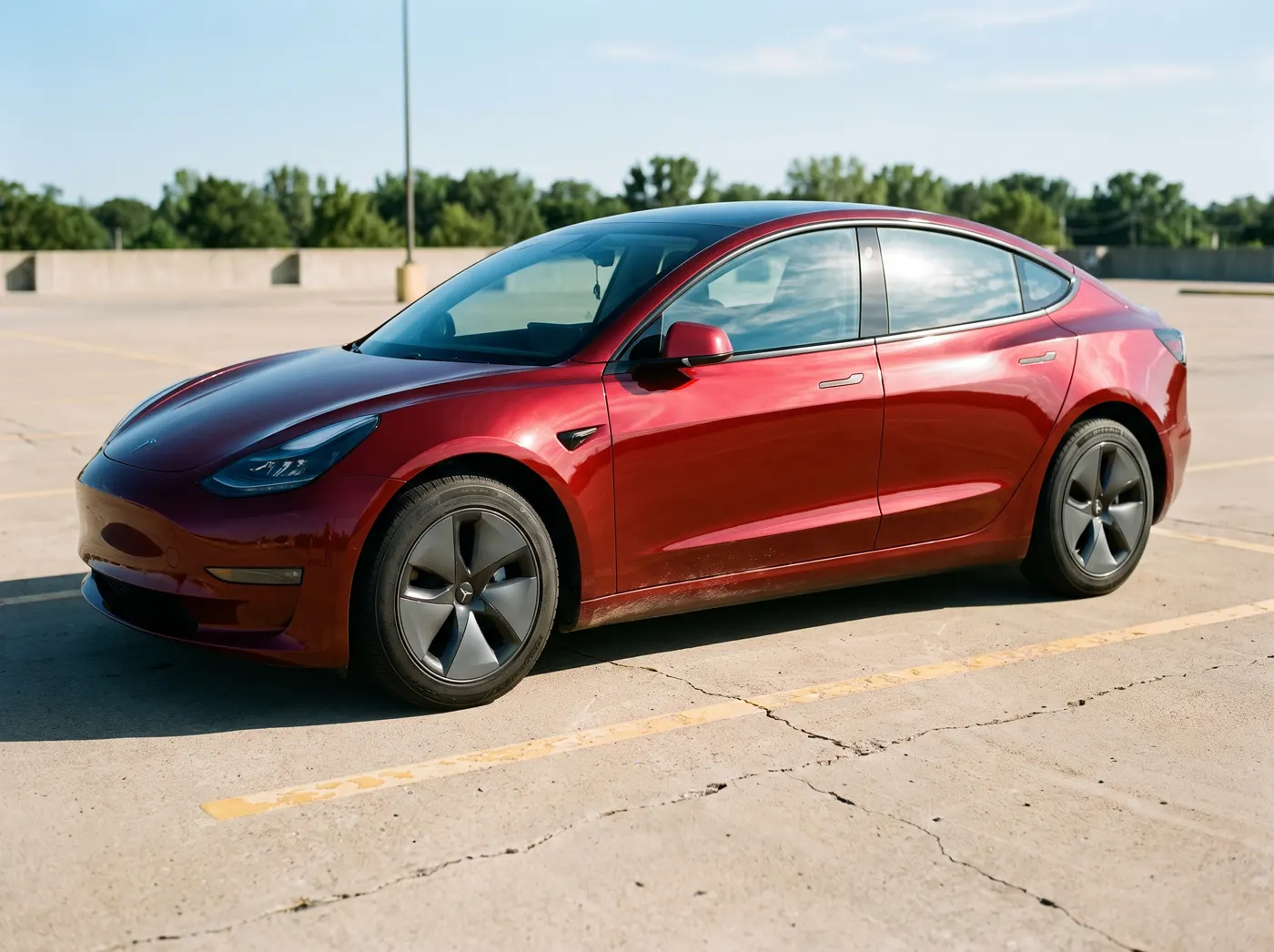 A Tesla Model 3 in gloss red vinyl with all exterior chrome trim blacked out.