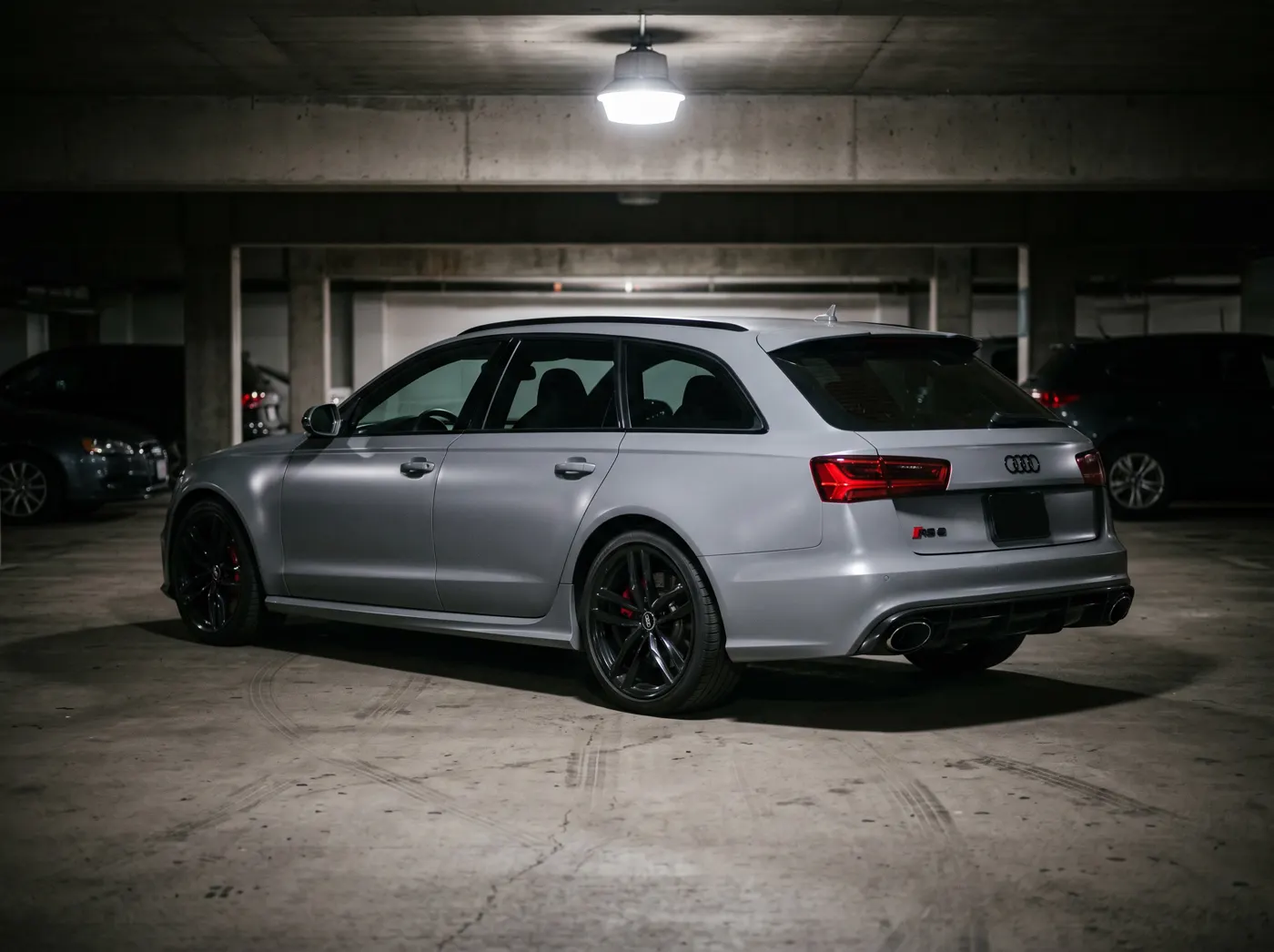 An Audi RS6 Avant in satin nardo gray vinyl, lit by a single overhead light in a garage.