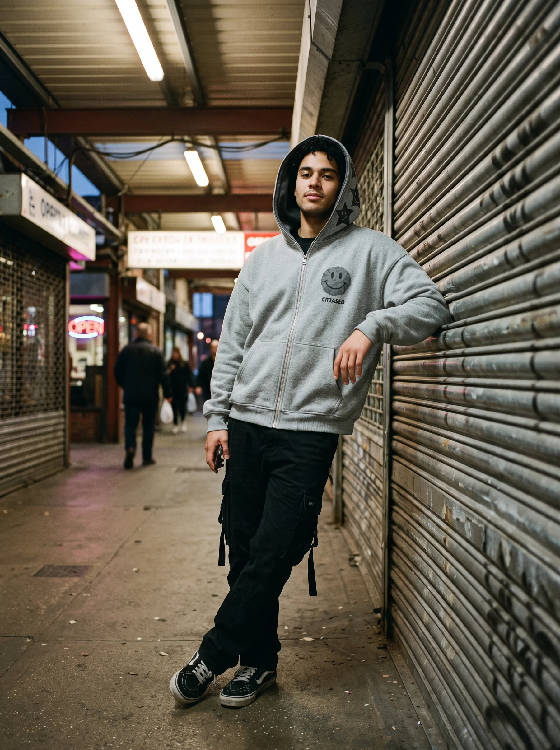 Model leaning on a metal shutter in the Heather zip hoodie with the star-face lining showing