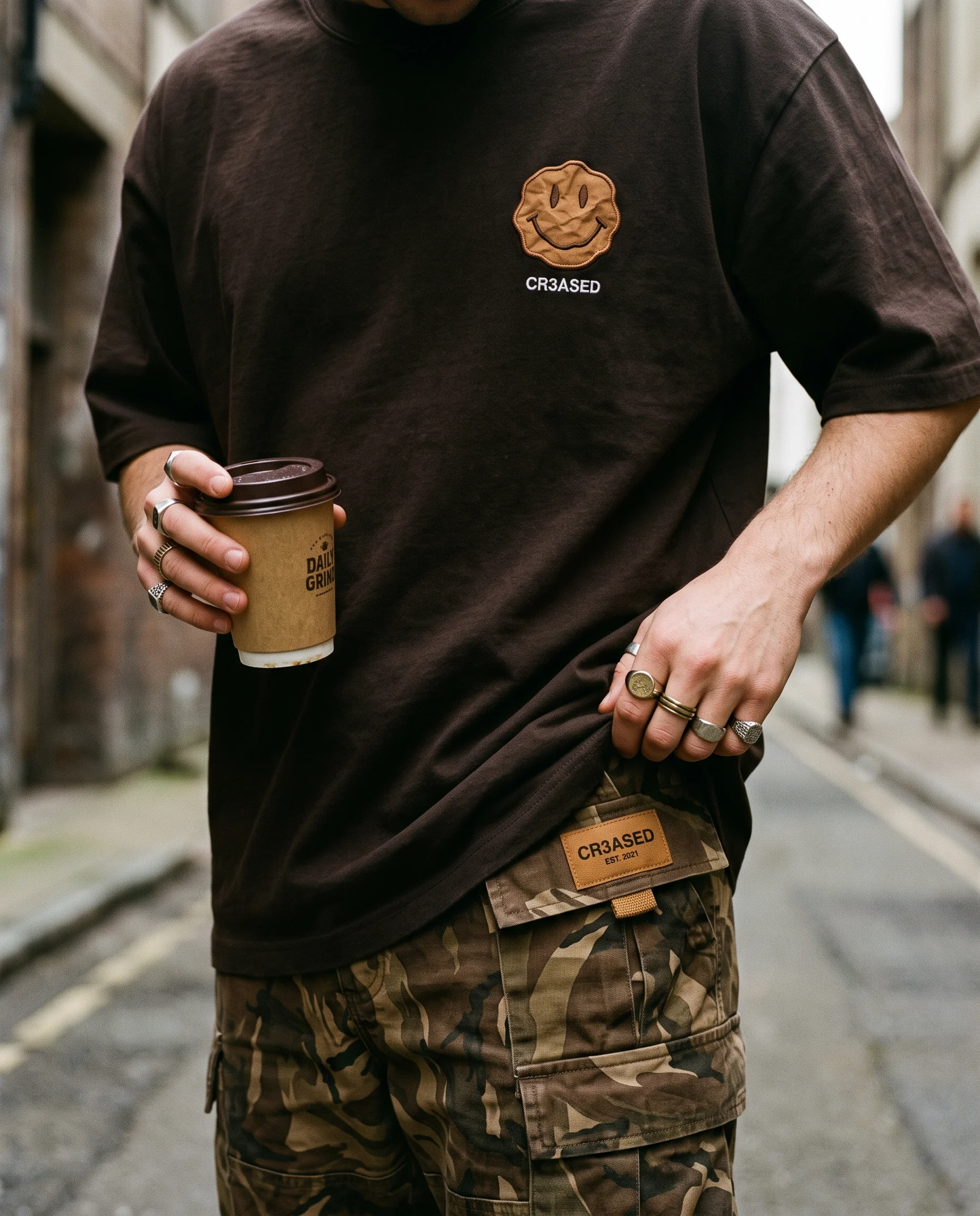 Hands adjusting the caramel label on Mocha camo cargos, coffee cup in hand